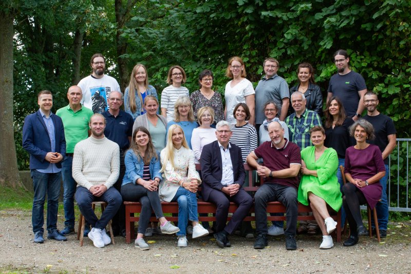 Das Kollegium der Nardini-Realschule im Freien vor einer Hecke, rund dreißig Lehrkräfte in drei Reihen; die vordere sitzt auf einer Holzbank.