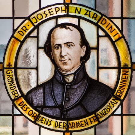 Kirchenfenster mit dem Bildnis Paul Josef Nardinis im Priestergewand. Die Umschrift lautet „Dr. Joseph Nardini — Gründer des Ordens der Armen Franziskanerinnen“.